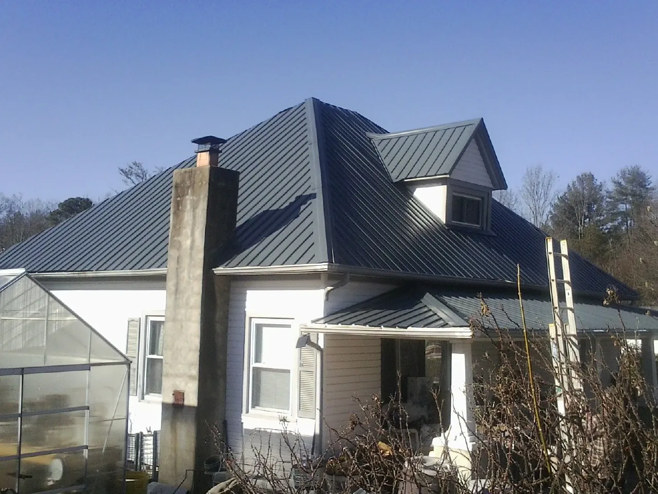 Dark blue standing seam metal roof on a white farmhouse with dormer — Slate & Tile Roof Repair by Roofing Brothers in Bushwood