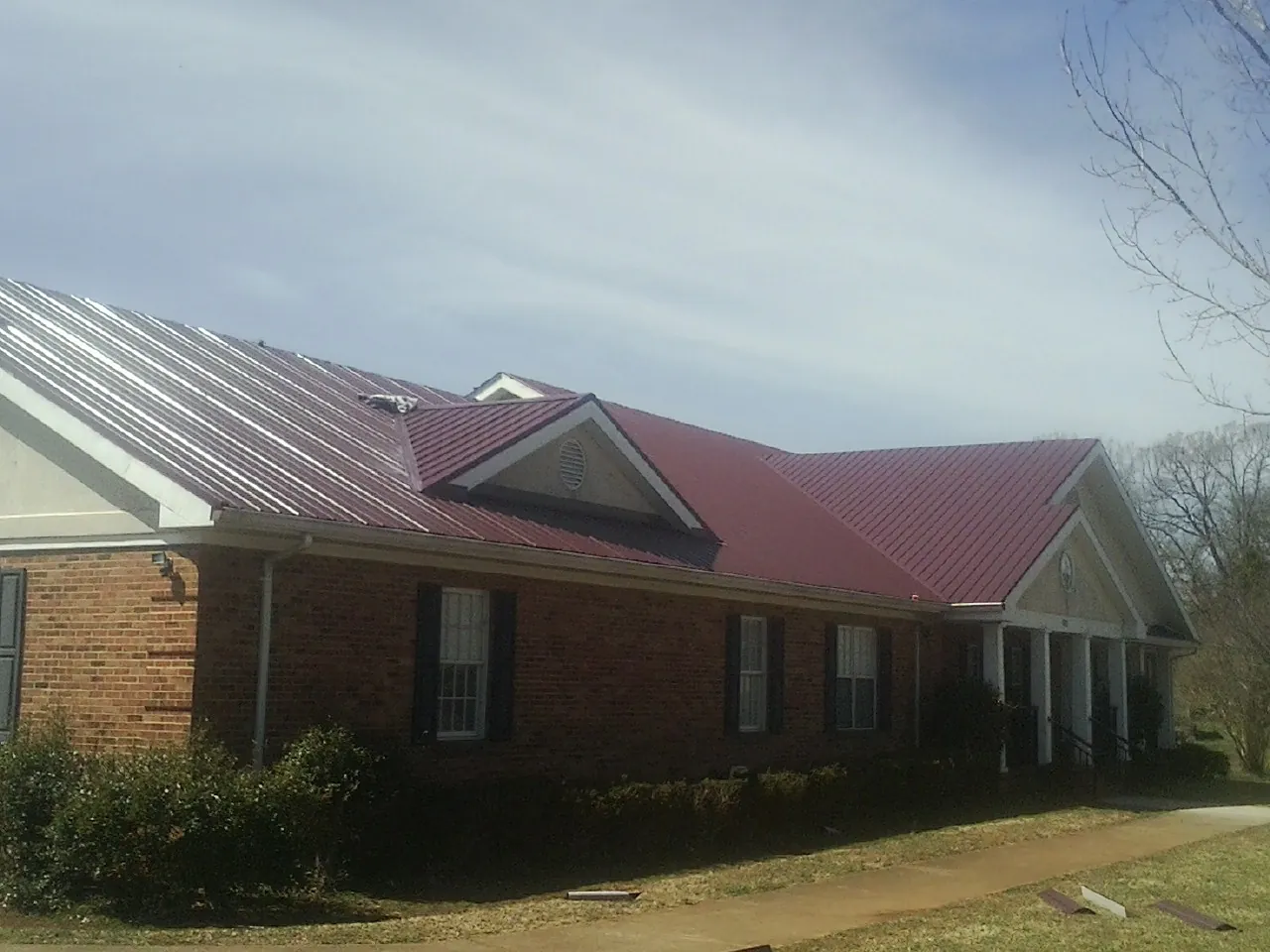 Red metal roof with gabled entries on a long brick building, from a Hail Damage Roof Repair job in Bushwood