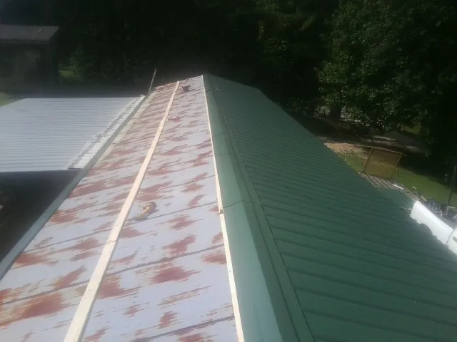 Old rusted panels beside newly installed green metal roofing — Wind Damage Roof Repair by Roofing Brothers in Bushwood
