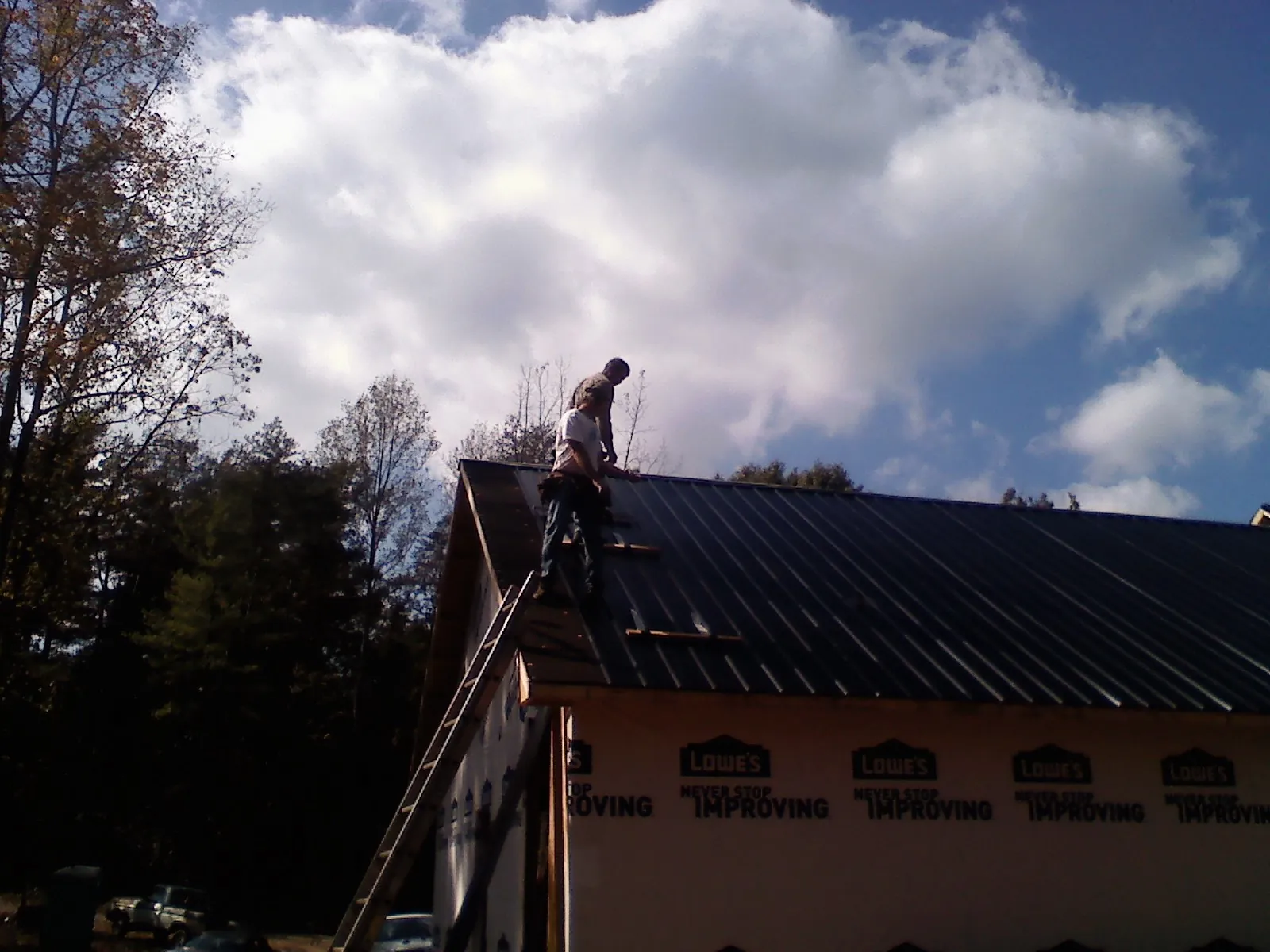 Roofer fastening dark metal panels high against a cloudy sky, from a Roof Inspection job in Bushwood