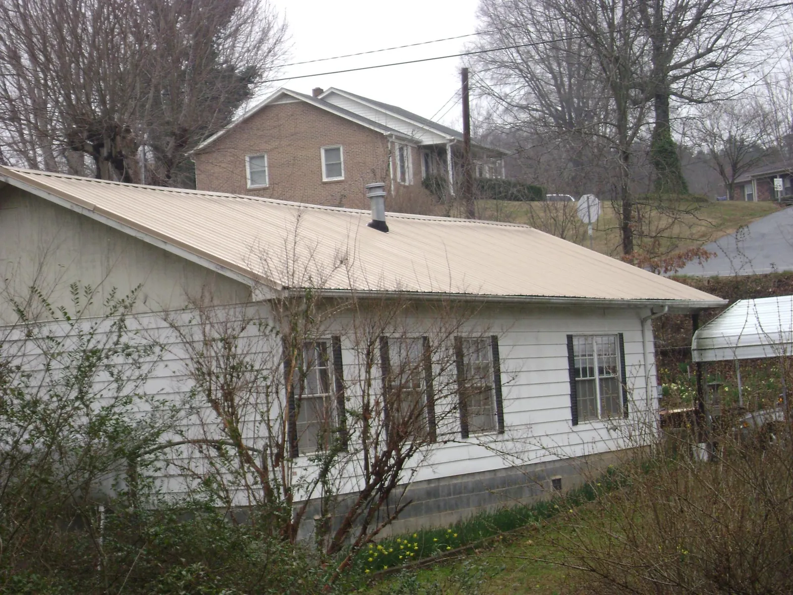 Tan metal roof on a white sided house set into a hillside — Commercial Roofing by Roofing Brothers in Bushwood