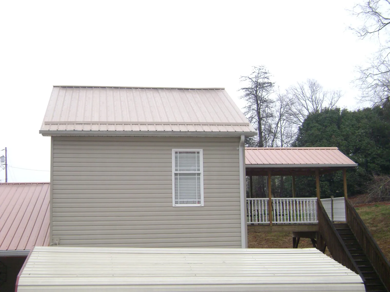 Tan metal roofs on a two story addition and attached porch, from a Roof Replacement job in Bushwood